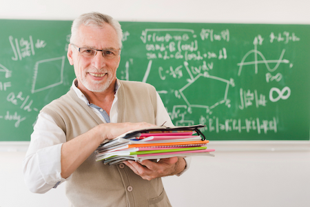 Professor Sean Widnall smiling and holding some book in front of a blackboard.