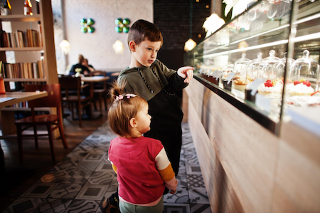 Boy and his todler sister looking at the selection fresh food at cafe counter.