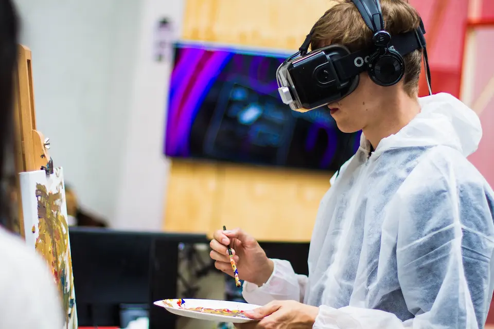 Boy wearing a VR headset while painting with a paintbrush on a white canvas.