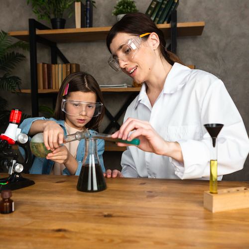 Woman and girl in protective glasses pour liquids into a flask together. 
